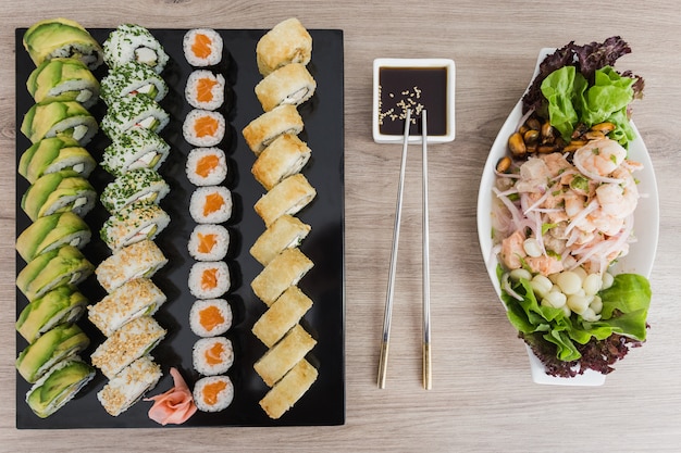 Rolos de sushi com ceviche e molho de soja em uma mesa de madeira