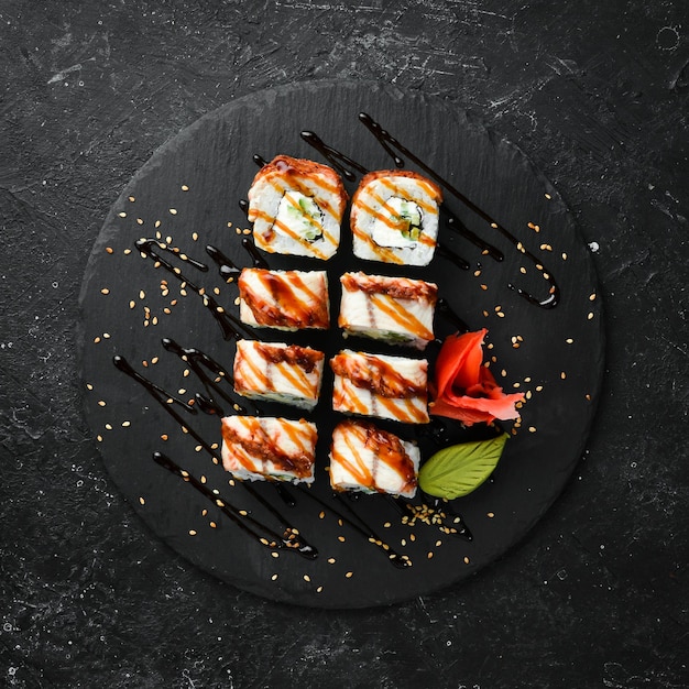 Rolos de sushi com pepino de enguia e queijo em uma placa de pedra preta Cozinha japonesa Vista superior
