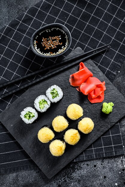 Rolos de sushi com pepino, salmão e camarão em uma bandeja de pedra.