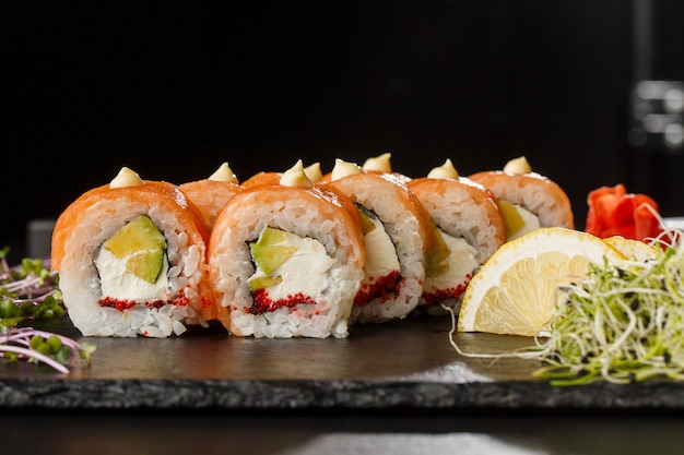 Rolos de sushi com salmão, abacate, caviar de peixe voador e cream cheese dentro no preto