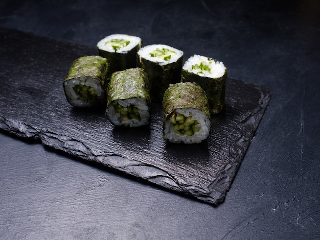 Rolos de sushi com salmão coberto de nori em fundo escuro. Cozinha oriental e conceito de comida tradicional