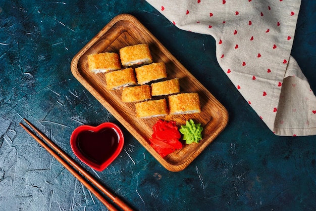 Foto rolos de sushi de tempura fritos colocados em placa de madeira em fundo escuro comida tradicional japonesa st