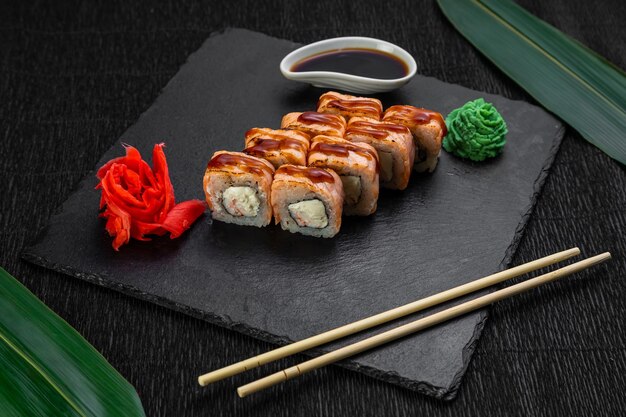 Rolos de sushi dispostos em um fundo escuro decorado com folhas de bambu e pauzinhos