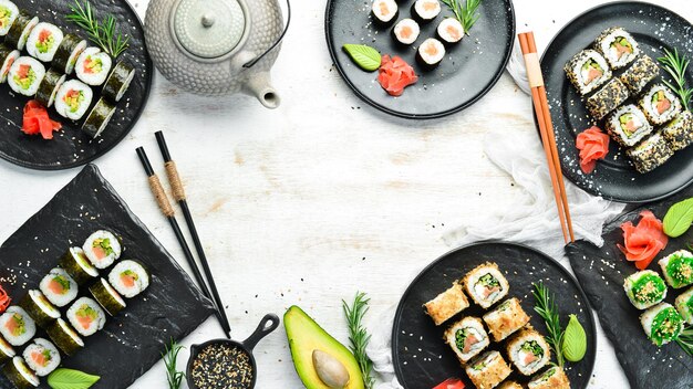 Rolos de sushi e bule com chá em fundo branco de madeira Grande conjunto de comida japonesa