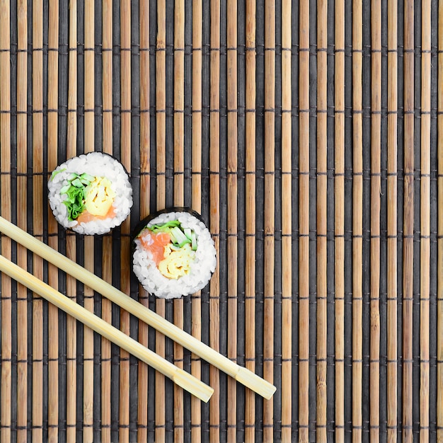 Rolos de sushi e pauzinhos de madeira encontram-se em uma esteira de serwing palha de bambu