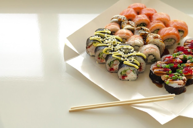Foto rolos de sushi em caixa de papel descartável em mesa branca serviço de entrega japão comida em conceito de recipiente