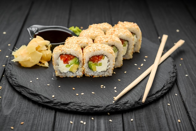 Rolos de sushi em gergelim com abacate, salmão e cream cheese em um preto