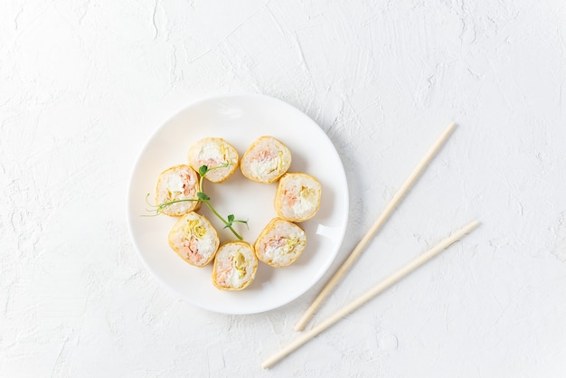 Rolos de sushi em um prato branco com pauzinhos.