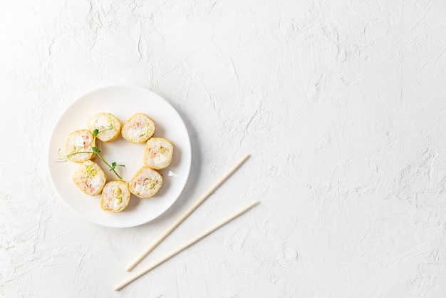 Rolos de sushi em um prato branco com pauzinhos.