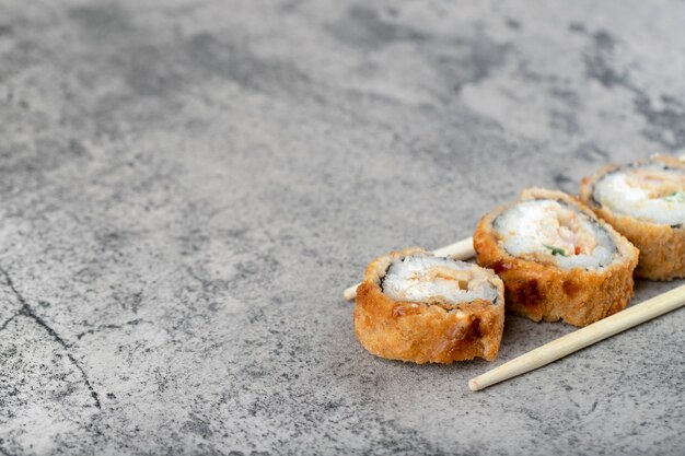 Rolos de sushi frito quente com pauzinhos de madeira descartáveis na mesa de pedra.