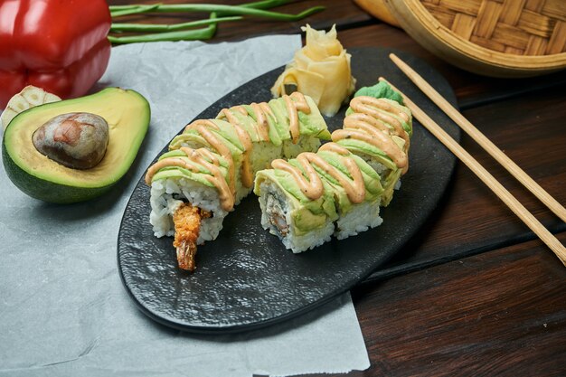 Rolos de sushi japonês clássico com camarão e abacate. Rolo de Califórnia em um prato preto com pauzinhos. Cozinha japonesa. Frutos do mar saudáveis