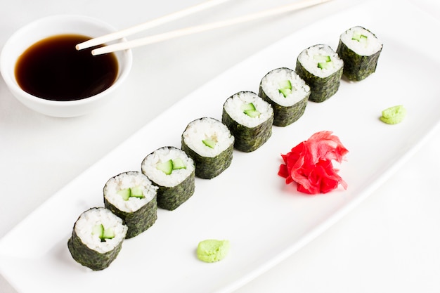 Rolos de sushi japonês com pepino, servindo com molho de soja, wasabi e gengibre no fundo branco