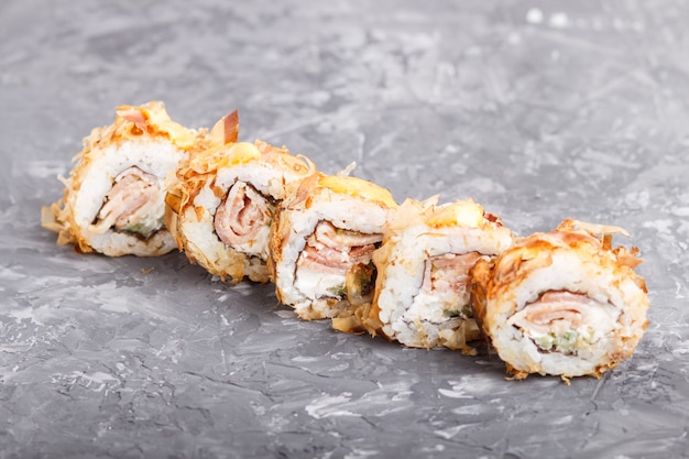 Foto rolos de sushi maki japonês com atum, pepino, queijo na superfície de concreto preto. vista lateral.