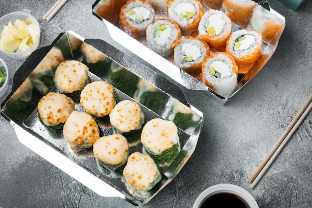 Rolos de sushi saborosos em caixas descartáveis em fundo de pedra cinza