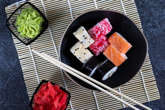 Rolos de sushi variados estão em uma placa preta e esteira de bambu em um fundo escuro