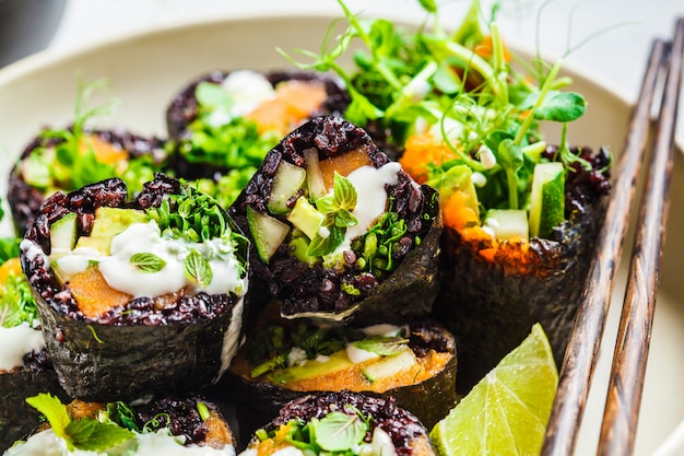 Foto rolos de sushi vegan com arroz preto, abacate e batata doce no prato branco
