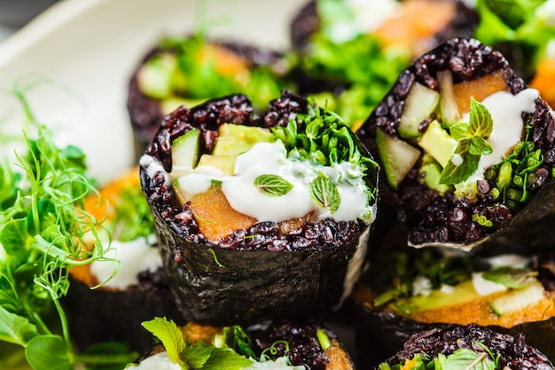 Rolos de sushi vegan com arroz preto, abacate e batata doce no prato branco