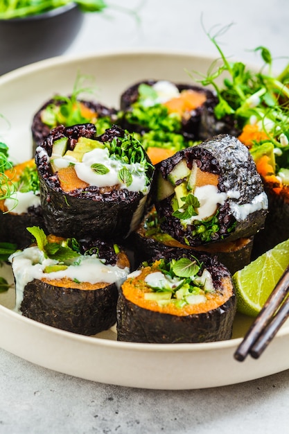 Rolos de sushi vegan com arroz preto, abacate e batata doce no prato branco