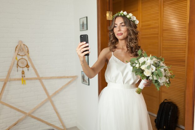 Romântica e feliz noiva caucasiana em elegante vestido de noiva tomando selfie