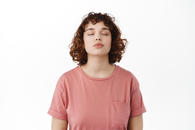 Romântica linda jovem fecha os olhos, esperando o beijo com os lábios franzidos, sonhando acordado em beijar alguém, de pé contra um fundo branco.