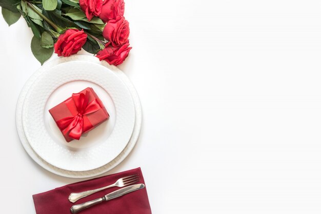 Romántica mesa con ramo de rosas rojas y regalo.