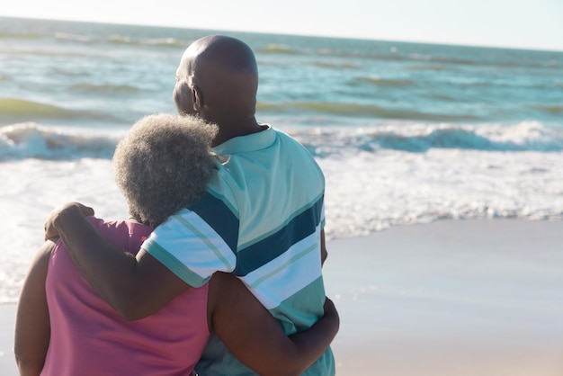 Romántica pareja de ancianos afroamericanos con los brazos alrededor mirando el hermoso paisaje marino bajo el cielo. Copiar espacio, playa, verano, inalterado, vacaciones, amor, juntos, jubilación, disfrute y naturaleza.