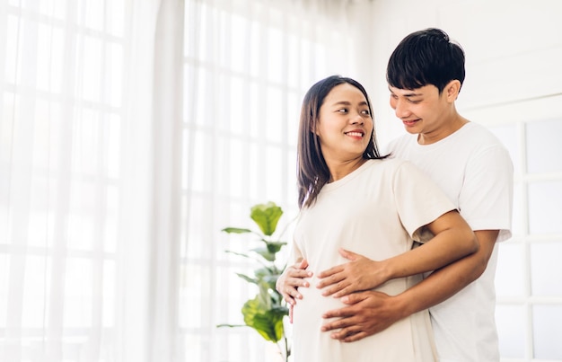 Romántica pareja asiática dulce marido abrazando y sonriendo belleza mujer embarazada asiática. Hombre esperando con mujer embarazo sostener al bebé en el vientre en casa