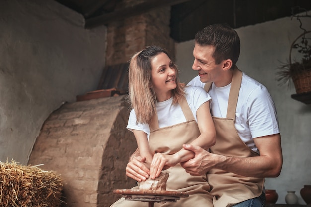 Romántica pareja de enamorados trabajando juntos en la rueda de alfarero y esculpiendo vasija de barro