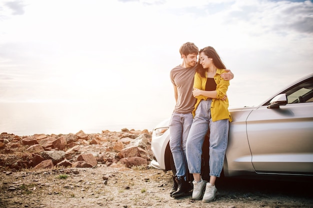 Foto romántica pareja joven y atractiva viendo la puesta de sol y besos con coche deportivo.