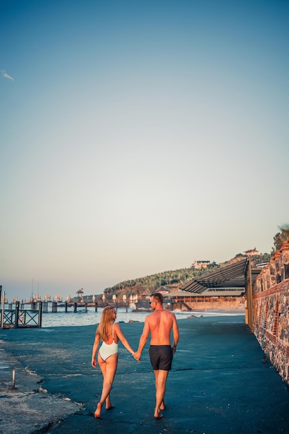 Romántica pareja joven enamorada caminando juntos al atardecer a lo largo de la playa mediterránea Vacaciones de verano en un país cálido Feliz pareja casada de vacaciones en Turquía Enfoque selectivo