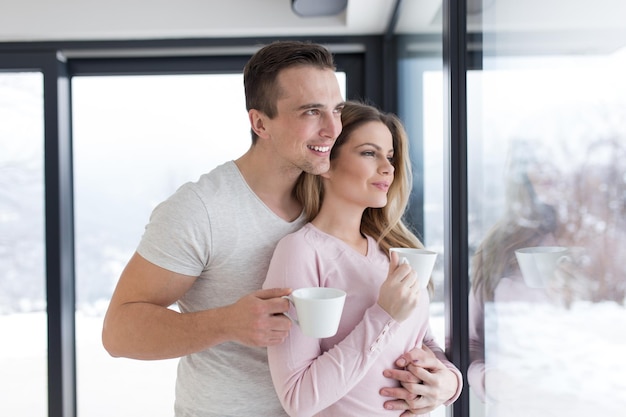 romántica pareja joven feliz disfrutando del café de la mañana junto a la ventana en el frío día de invierno en casa