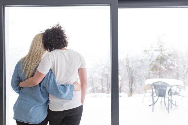 Foto romántica pareja joven feliz disfrutando del café de la mañana junto a la ventana en el frío día de invierno en casa