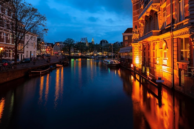 Romántica vista nocturna de Amsterdam Edificios, automóviles y barcos reflejados en el agua.