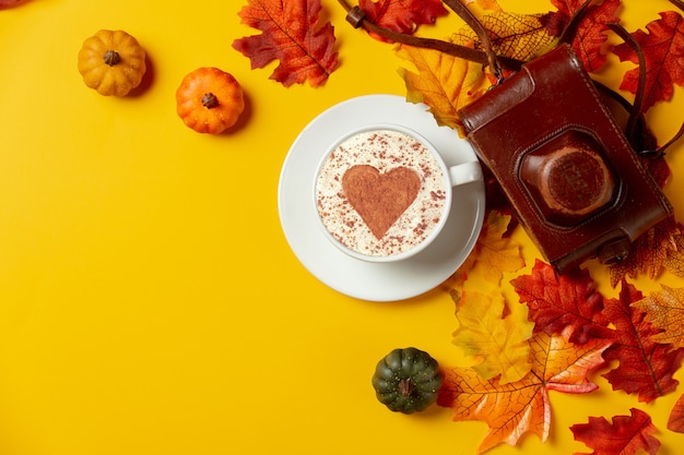 Romântica xícara de café com folhas de outono de câmera vintage em fundo amarelo. vista do topo