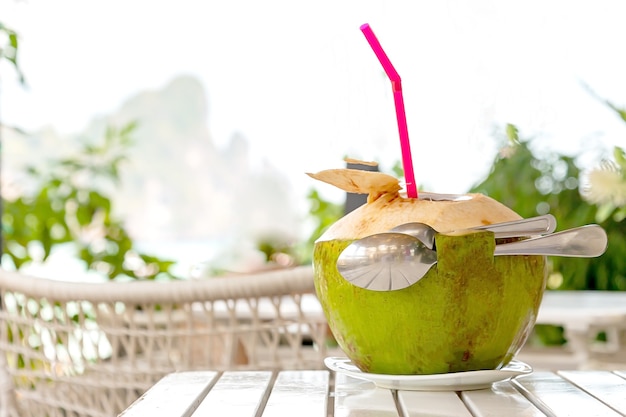 Foto romântico para dois suco de coco fresco com canudo e duas colheres na mesa de madeira branca praia borrada