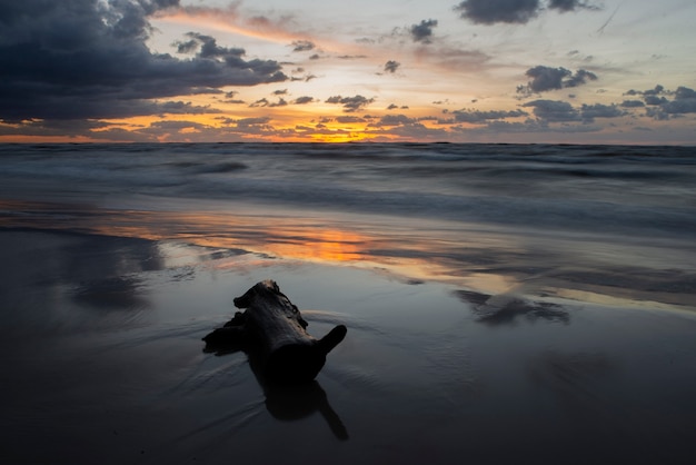 Romântico pôr do sol na praia com madeira na areia