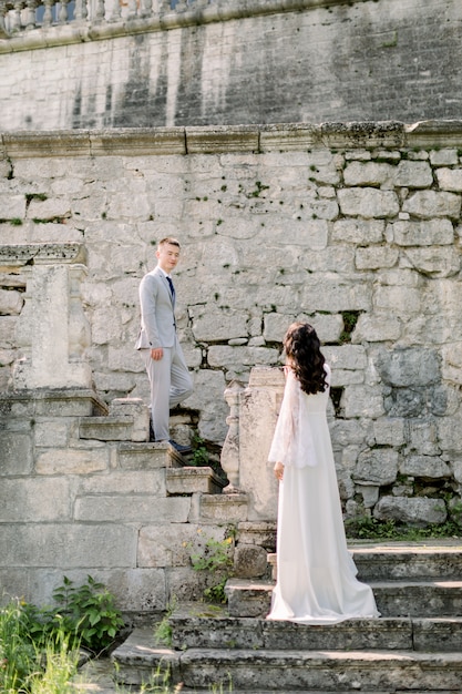 Romántico retrato de boda al aire libre de la hermosa pareja de recién casados chinos de pie en las escaleras del antiguo castillo