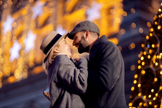 Románticos amantes de la Navidad tomados de la mano y riendo al aire libre en Nochebuena