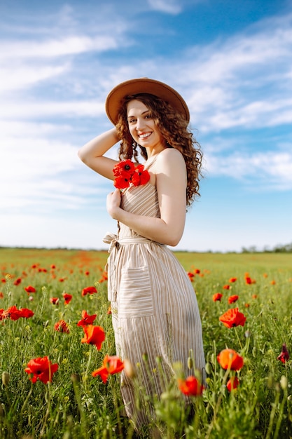 Romantische Frau mit Blume in der Hand, die in einem Mohnfeld bleibt