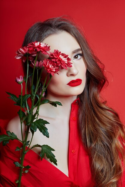 Romantische Frau mit langen blonden Haaren und Blumen in ihren Händen in einem roten Kleid, glatte saubere Haut