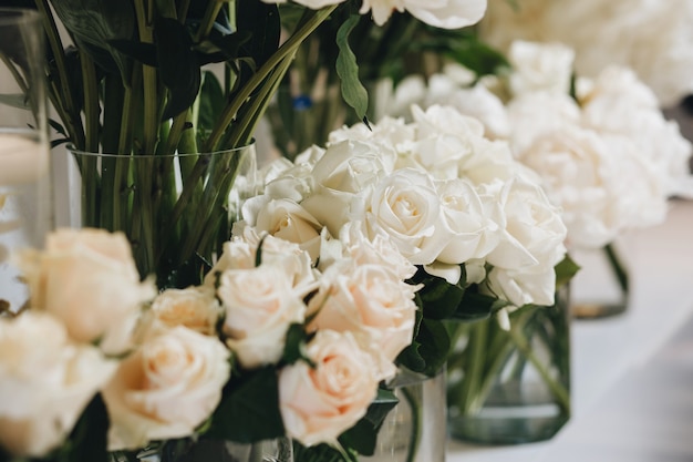 Romantische Hochzeitstischdekoration mit großen, üppigen Blumensträußen, darunter weiße Rosen, Ranunkeln, persische Butterblumen, weiße Orchideen und Kerzen