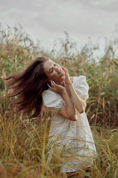 Romantische junge Frau im dichten hohen Gras im Feld Verträumte sanfte Frau in einem weißen Kleid in der Natur Natürliche Schönheit Lebensfreude