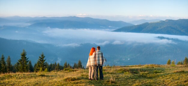 Romantische Paare, die auf einem Hügel genießt einen Morgendunst über den Bergen stehen. Rückansicht. Panorama