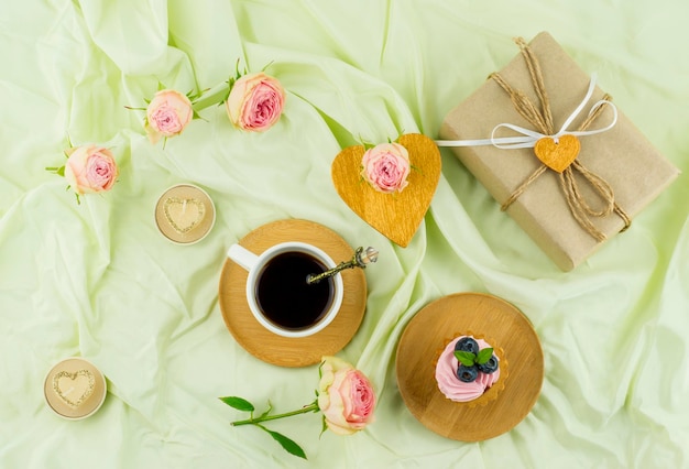 Romantische schöne Komposition zum Valentinstag. eine Tasse Kaffee, ein Cupcake mit Obst und Sahne, Kerzen, Rosenknospen. ein Geschenk auf einem pastellfarbenen Hintergrund.