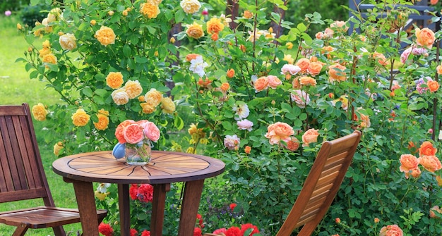 Romantische Sitzecke im Rosengarten Runder Holztisch und Stühle neben den großen blühenden Sträuchern englischer Rosen