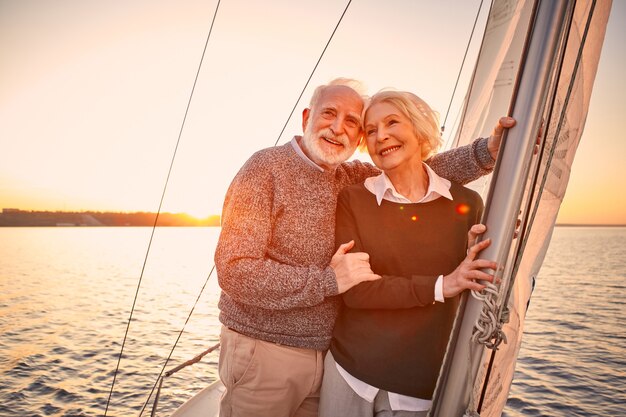 Romantischer Abend auf dem Boot glückliches Seniorenpaar umarmt und genießt den atemberaubenden Sonnenuntergang im Stehen