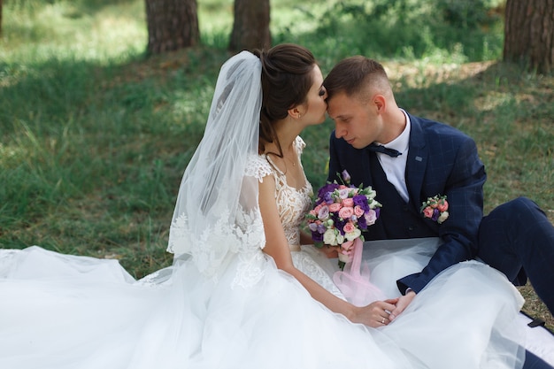 Romantischer Hochzeitsmoment. Glückliche junge Hochzeitspaare, die draußen im grünen Park umarmen. emotionale Braut im weißen Kleid und Bräutigam in der Klage im Weg im Frühjahr.