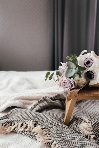 Romantischer Morgen. Couchtisch aus Holz mit Blumen auf dem Bett mit Decke. Fliederrosen mit Eukalyptus und Anemonen. Innengrautöne.