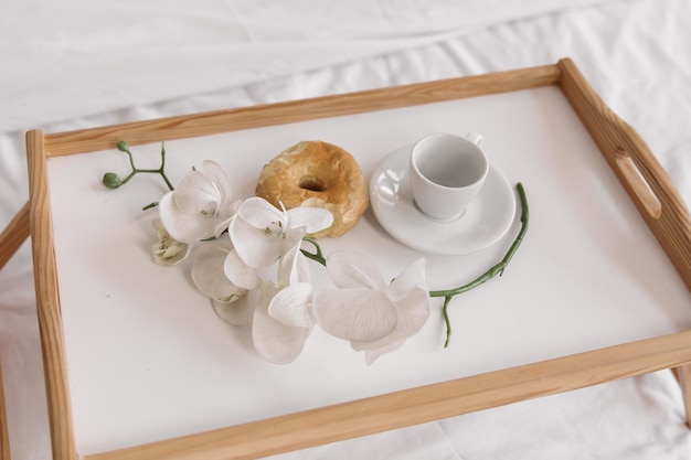 Romantischer Morgen. Couchtisch aus Holz mit Blumen auf dem Bett mit Plaid, Kaffeetasse, Blumen und Donut.