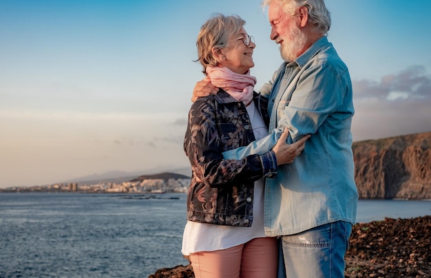 Romantisches älteres Paar, das sich umarmt und in die Augen schaut, die bei Sonnenuntergang auf See stehen